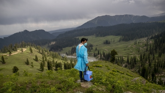 Nazir Ahmed, a healthcare worker, carries vaccines and looks out from a hillock for shepherds to vaccinate them against Covid-19 in Tosamaidan, southwest of Srinagar on June 21. Fueled by misinformation and mistrust, many residents, particularly in remote rural areas, believe that vaccines cause impotence, serious side effects and could even kill. Some simply say they do not need the shots because they’re immune to the coronavirus.(Dar Yasin / AP)