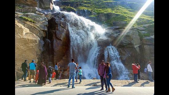 Tourists stop at a waterfall at Khoksar in Lahaul and Spiti district on Friday. there has been a surge in tourist inflow lately after the state government relaxed Covid-19 curbs. (PTI)