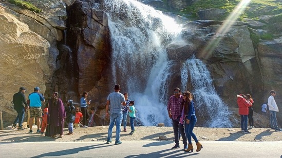 Tourists who made a pit-stop at a waterfall at Khoksar in Lahual Spiti district on July 9. In Himachal Pradesh, the growing rush of tourists, particularly during the weekends, has pushed the state government to deploy additional police personnel in hill stations.(PTI)