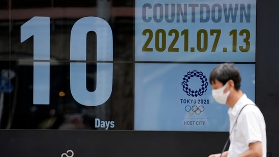 A man wearing a face mask against the spread of the coronavirus walks in front of a countdown calendar showing 10 days to start Tokyo 2020 Olympics.(AP)