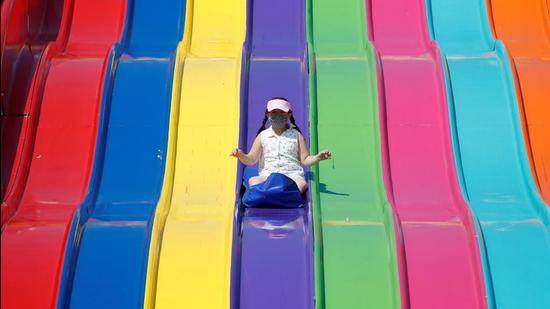 A young girl wearing a mask slides down on a ride as the Calgary Stampede festivities get underway following a year off due to Covid-19 restrictions, in Calgary, Alberta, Canada July 9, 2021. (REUTERS)