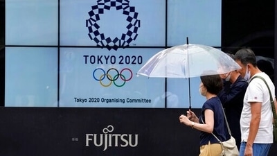 People wearing face masks walk past the logo of the Tokyo 2020 Olympic Games near the Shimbashi train station. (AP)