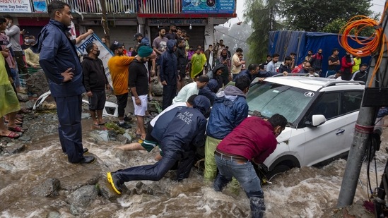 People help dislodge a car stuck due to flash floods after heavy monsoon rains in Bhagsunag, Himachal Pradesh on July 12. Videos on social media also showed vehicles being swept away by flash floods in the popular tourist town on McLeodganj.(Ashwini Bhatia / AP)