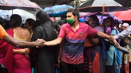 Residents forming a human chain as others queue in the rain to get inoculated against Covid-19, at Dharavi in Mumbai on July 10. A delayed monsoon has also meant that farmers in much of northwest India had to halt sowing their summer crops, raising the possibility of some impact on yields in a year when the economy has, for the second time, suffered due to the pandemic.(Satish Bate / HT Photo)