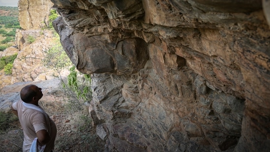 A man looking at a wall in a cave it the Aravalli mountain range in Haryana on July 10. Archaeologists are viewing the paintings in continuation with the Soanian culture which has been found in Shivalik hills, Narmada and Aravallis, Bhattacharyya said.(Sanchit Khanna / HT Photo)