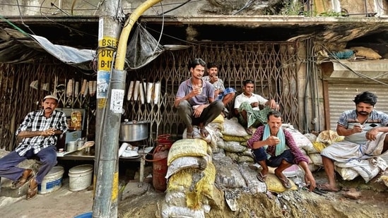 The tea things are arranged on the shuttered grills of a building’s characterless back-wall, while the customers sit atop a mound of cement sacks that have solidified into a rock-like hard surface. (Mayank Austen Soofi)