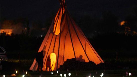 A man stands by a teepee surrounded by solar lights and flags that now mark the spots where 751 human remains were recently discovered in unmarked graves at the site of the former Marieval Indian Residential School on the Cowessess First Nation in Saskatchewan on June 27, 2021. (AFP) A man stands by a teepee surrounded by solar lights and flags that now mark the spots where 751 human remains were recently discovered in unmarked graves at the site of the former Marieval Indian Residential School on the Cowessess First Nation in Saskatchewan on June 27, 2021. (AFP)