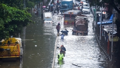 People crossing a waterlogged street at Parel after heavy rain in Mumbai on July 18. Chief Minister Uddhav Thackeray has said that people living on the Mithi river bank and other places close to the shore should be evacuated early. He also asked authorities to ensure medical facilities in jumbo Covid-19 centres were not affected because of the heavy rain. (Shashank Parade / PTI) People crossing a waterlogged street at Parel after heavy rain in Mumbai on July 18. Chief Minister Uddhav Thackeray has said that people living on the Mithi river bank and other places close to the shore should be evacuated early. He also asked authorities to ensure medical facilities in jumbo Covid-19 centres were not affected because of the heavy rain. (Shashank Parade / PTI)