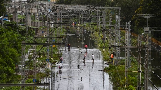 Commuters walk on waterlogged railway tracks following heavy rain, at Kurla in Mumbai on July 18. Several areas in the city have been flooded after heavy rainfall over the last 24 hours and suburban train services were also disrupted, crippling movement.(Kunal Patil / PTI)