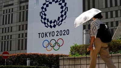 A woman wearing a protective mask walks with an umbrella to shield from the sun walks in front of a Tokyo 2020 display at Tokyo Metropolitan government building at the 2020 Summer Olympics, Tuesday, July 20, 2021, in Tokyo (AP) A woman wearing a protective mask walks with an umbrella to shield from the sun walks in front of a Tokyo 2020 display at Tokyo Metropolitan government building at the 2020 Summer Olympics, Tuesday, July 20, 2021, in Tokyo (AP)