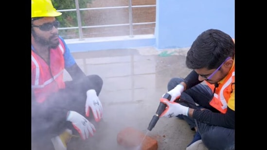 The image shows two men trying to cut a brick with a waterjet.(YouTube/@Crazy XYZ) The image shows two men trying to cut a brick with a waterjet.(YouTube/@Crazy XYZ)
