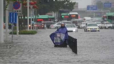 A resident wearing a rain cover stands on a flooded road in Zhengzhou, Henan province on July 20, 2021. (via Reuters)