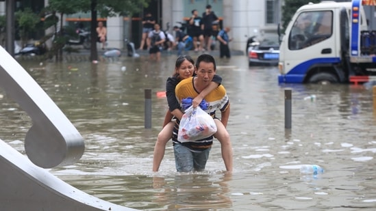 A man carrying a woman wades through a flooded road following heavy rainfall in Zhengzhou, Henan province, China via REUTERS (VIA REUTERS)