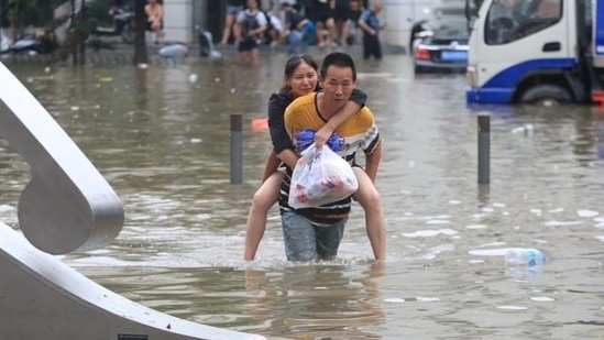 A man carrying a woman wades through a flooded road following heavy rainfall in Zhengzhou, Henan province, China July 21, 2021. China Daily via REUTERS(VIA REUTERS)