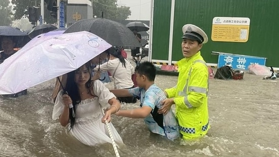 A traffic police officer guides residents to cross a flooded road with a rope during heavy rainfall in Zhengzhou, Henan province, China via REUTERS(VIA REUTERS)