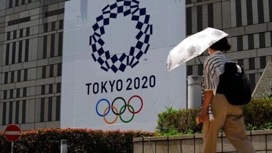 A woman wearing a protective mask walks with an umbrella to shield from the sun walks in front of a Tokyo 2020 display.(AP) A woman wearing a protective mask walks with an umbrella to shield from the sun walks in front of a Tokyo 2020 display.(AP)