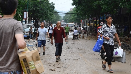 Residents carry food and living necessities on a muddy street in Gongyi city as torrential rain lashed China's central province of Henan on July 21.(Photo by JADE GAO/AFP)