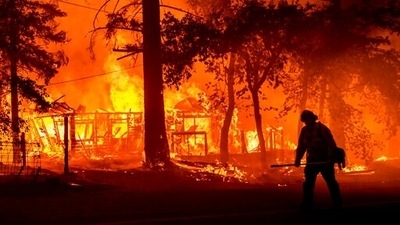 Firefighter passes a burning home as the Dixie Fire flares in Plumas County, California. (AP)