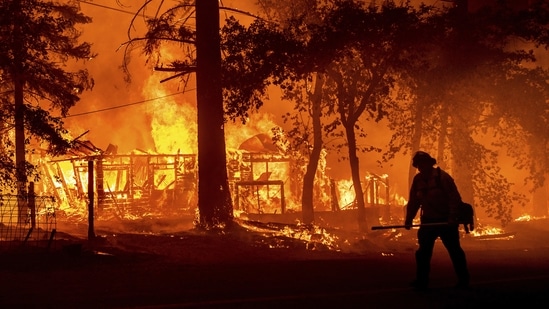 A firefighter passes a burning home as the Dixie Fire flares in Plumas County, California on July 24. Around 5,400 firefighters have been struggling to contain the inferno, which was just 22% contained late July 26, AFP reported citing the California fire and forestries department reported.(Noah Berger / AP)