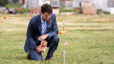 Canadian Prime Minister Justin Trudeau lays a teddy bear at a small flag in a field prior to a ceremony at the site of a former residential school where ground-penetrating radar detected a potential 751 unmarked graves, in Cowessess First Nation, Saskatchewan, Canada on July 6, 2021. (REUTERS/FILE) Canadian Prime Minister Justin Trudeau lays a teddy bear at a small flag in a field prior to a ceremony at the site of a former residential school where ground-penetrating radar detected a potential 751 unmarked graves, in Cowessess First Nation, Saskatchewan, Canada on July 6, 2021. (REUTERS/FILE)