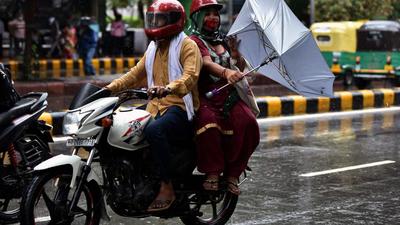 A pillion rider on a bike tries to hold an umbrella to protect herself from rainfall, in New Delhi on Wednesday, July 28. (ANI)