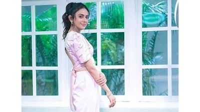 Rakul was seen wearing a pale pink crop top that had line drawings of faces all over it in grey, the top had a V-neck and puffed, half sleeves. The top was backless, and had pink fabric coming out of the back to tie as a bow. (Instagram) Rakul was seen wearing a pale pink crop top that had line drawings of faces all over it in grey, the top had a V-neck and puffed, half sleeves. The top was backless, and had pink fabric coming out of the back to tie as a bow. (Instagram)