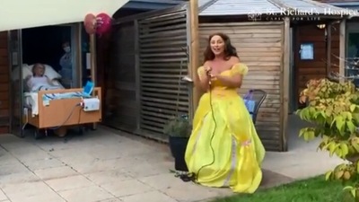 The image shows a singer singing for the 88-year-old woman on her birthday. (YouTube/@St Richard's Hospice)