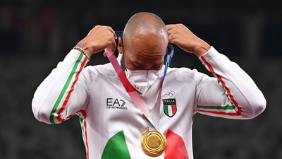 Tokyo 2020 Olympics - Athletics - Men's 100m - Medal Ceremony - Olympic Stadium, Tokyo, Japan - August 2, 2021. Gold medallist, Lamont Marcell Jacobs of Italy wearing a protective face mask on the podium places the medal around his neck REUTERS/Dylan Martinez (REUTERS)