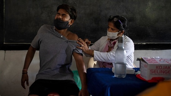 A man reacts as a health worker inoculates him against the coronavirus during a vaccination drive inside a classroom at a school in Noida.(AP)