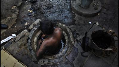 A municipal worker attempts to unblock a sewer overflowing with human excreta in New Delhi on October 7, 2009. (HT file photo)