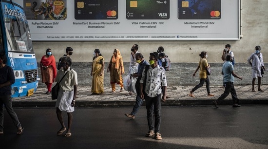 People wearing masks as a precaution against COVID-19 wait to board buses as others walk in Kochi, Kerala (AP)
