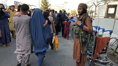 A member of Taliban stands guard as people walk at the entrance gate of Hamid Karzai International Airport in Kabul, Afghanistan. (REUTERS)