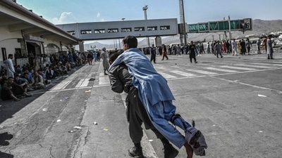 A volunteer carries an injured man as other people can be seen waiting at the Kabul airport. (AFP Photo) A volunteer carries an injured man as other people can be seen waiting at the Kabul airport. (AFP Photo)