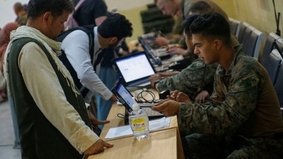 A U.S. Marine assigned to 24th Marine Expeditionary Unit checks in evacuees before their flight during an evacuation at Hamid Karzai International Airport. (via REUTERS)