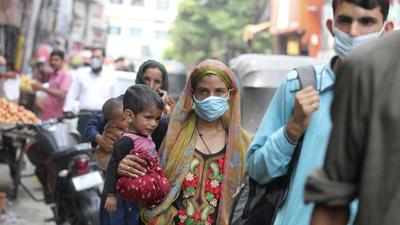 A woman wearing a face mask as a precaution against the coronavirus carries a child and walks in a market area in Jammu on Wednesday. (AP)