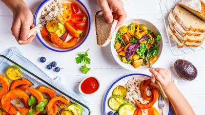 Flat lay of family hands eating healthy food. Vegan lunch table top view. Baked vegetables, fresh salad, berries, bread on a white background. (Getty Images/iStockphoto)