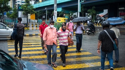 People wearing face masks as a precaution against Covid-19 walk at a pedestrian crossing in Kochi. (AP Photo) People wearing face masks as a precaution against Covid-19 walk at a pedestrian crossing in Kochi. (AP Photo)