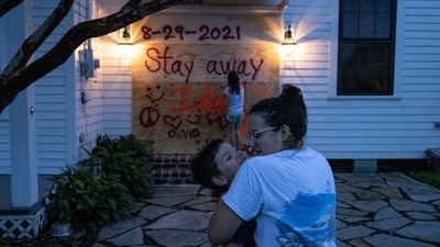A resident snuggles her son as her daughter places the finishing touches on a sign they painted after boarding up their property in preparation for Hurricane Ida in Morgan City, Louisiana, U.S. on August 28. (REUTERS)