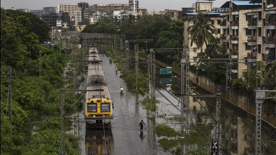 Commuters walk on the flooded railway track near Tilak Nagar station in Mumbai in July. Mumbai is one of the most vulnerable cities to the climate crisis-induced hazards such as sea-level rise, storm surge and urban flooding. These extreme weather events are only going to increase in the future. (HT Archive)