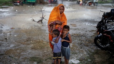 A woman stands with her children under-construction flyover amidst rainfall in New Delhi to receive a dose of Covid-19 vaccine. (REUTERS)