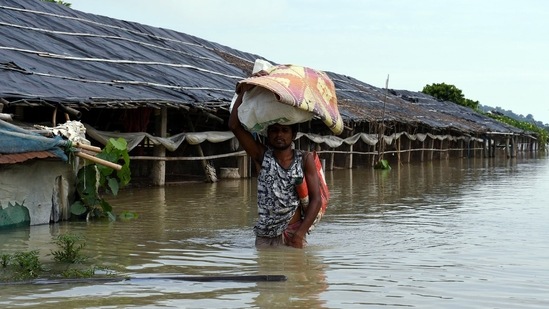 A man with his belongings wades through a flood-affected area due to heavy rainfall, in Morigaon on Monday. (ANI)