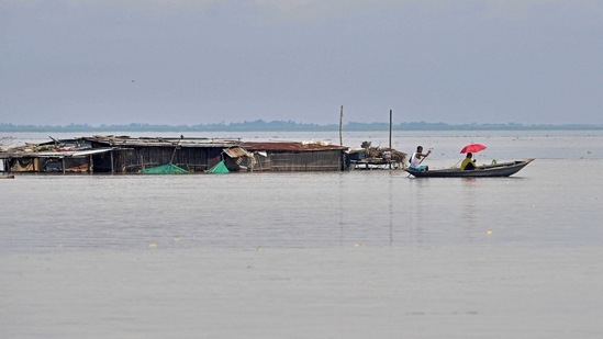 A villager rows a boat next to a partially submerged hut in a flood affected area of Morigaon district in Assam.(AFP)