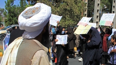 A member of the Taliban watches as Afghan women hold placards during a protest in Herat. (AFP Photo) A member of the Taliban watches as Afghan women hold placards during a protest in Herat. (AFP Photo)
