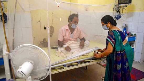 A relative attends to a family member inside the dengue ward of a government hospital, in UP. (PTI)