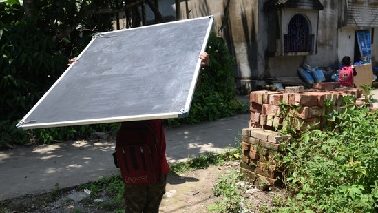 A child carries a blackboard while returning home after the special class organised by Towards Future, at a temporary market place in Kashinathpur Bazar, Rajarhat, West Bengal, on September 4.(Samir Jana / HT Photo)