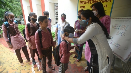 A teacher ties a face mask to a student before he enters the school in Noida.(Sunil Ghosh/HT Photo) A teacher ties a face mask to a student before he enters the school in Noida.(Sunil Ghosh/HT Photo)