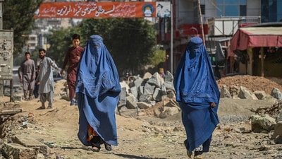 A banner with a picture of late Afghan commander Ahmad Shah Massoud is installed next to residential buildings as burqa-clad Afghan women walk along an under-construction road in Kabul. (AFP)