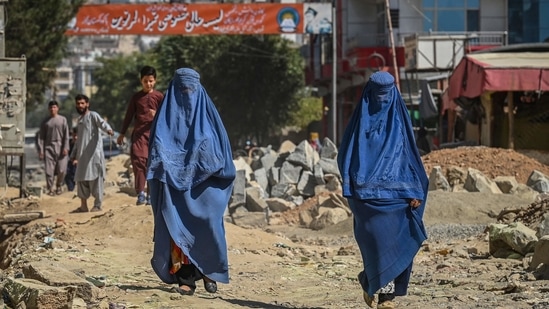 A banner with a picture of late Afghan commander Ahmad Shah Massoud is installed next to residential buildings as burqa-clad Afghan women walk along an under-construction road in Kabul. (AFP)