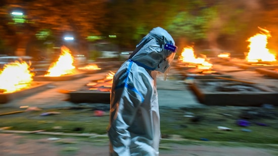 A man in PPE coveralls walks past funeral pyres of Covid-19 victims, at Sarai Kale Khan crematorium, in New Delhi, India, on April 28, 2021.&nbsp;(Amal KS/HT file photo)