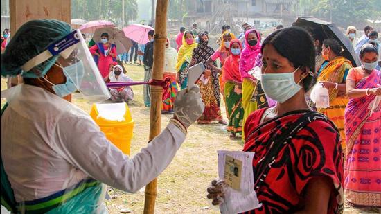 A health worker sanitises voters as they wait in queues to cast votes at a polling station. The BJP’s explicit attempts to communalise the UP polls by mobilising Hindus, and the Opposition’s implicit hope to do so by winning over Muslims, is dangerous. (PTI)